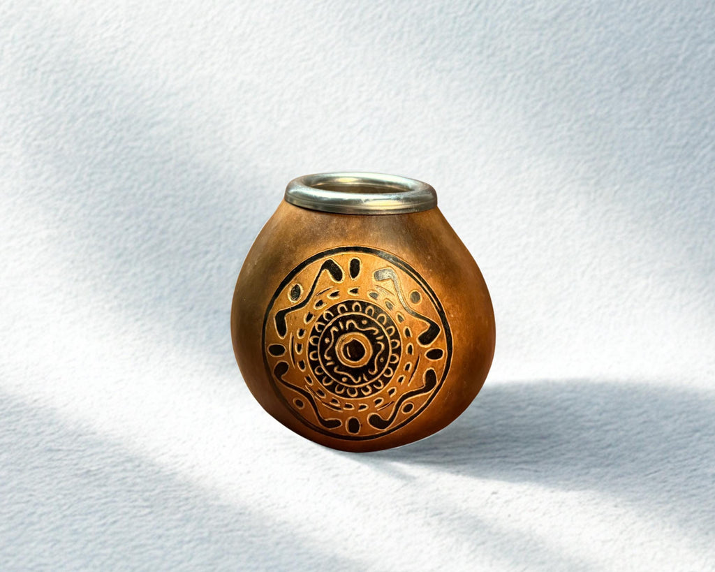 A small handcrafted clay pot with a metallic rim and intricate black geometric patterns on the front, set against a textured white background with soft shadows.