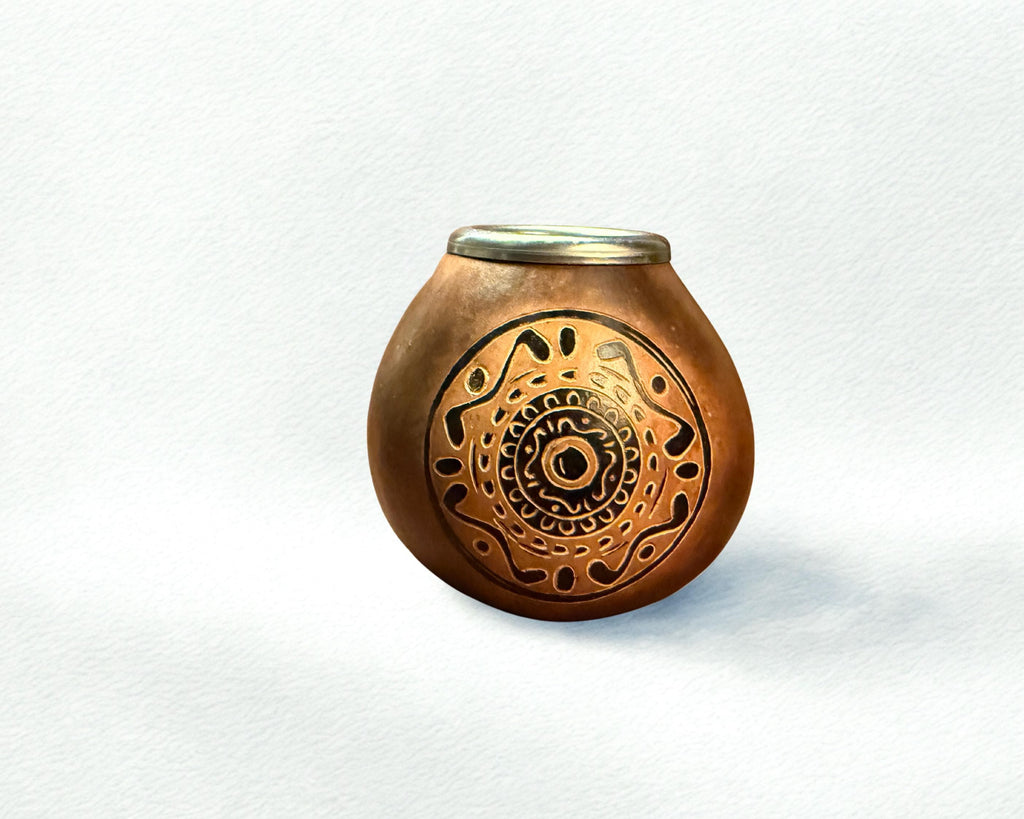 A small round copper-colored decorative pot with a lid, featuring an intricate circular cutout or etched mandala-like pattern on the front, set against a textured white background.