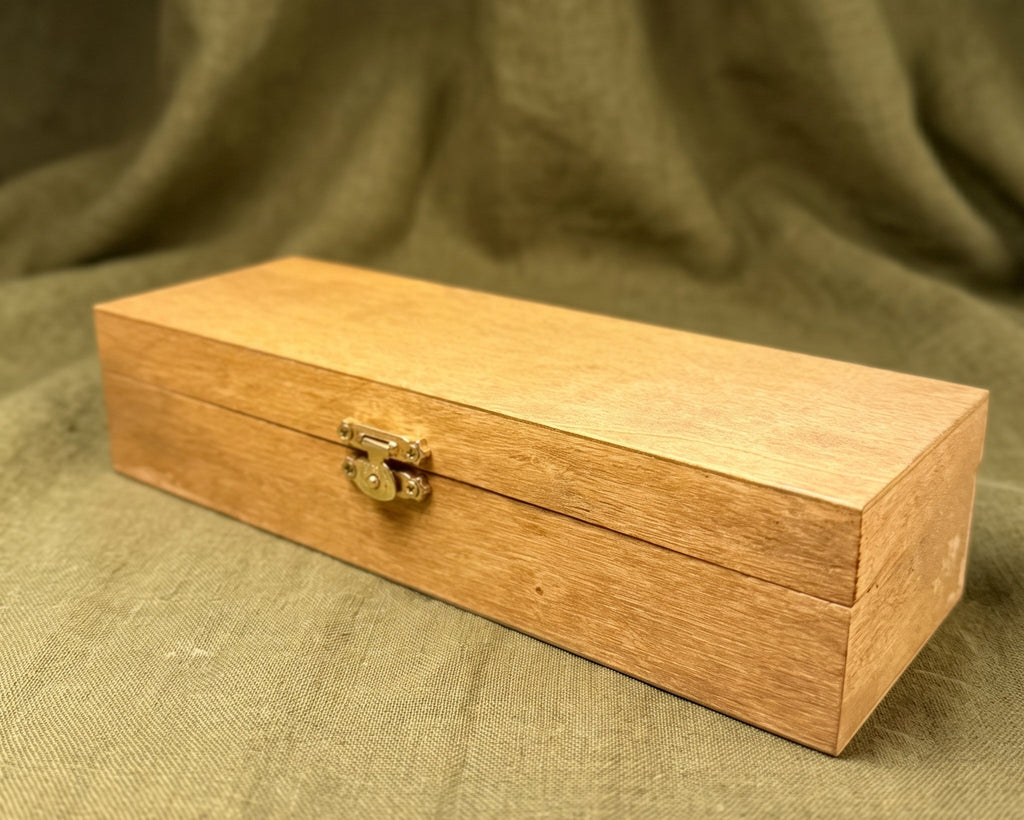 A rectangular light brown wooden box with a small brass clasp, resting on a draped olive green fabric background.